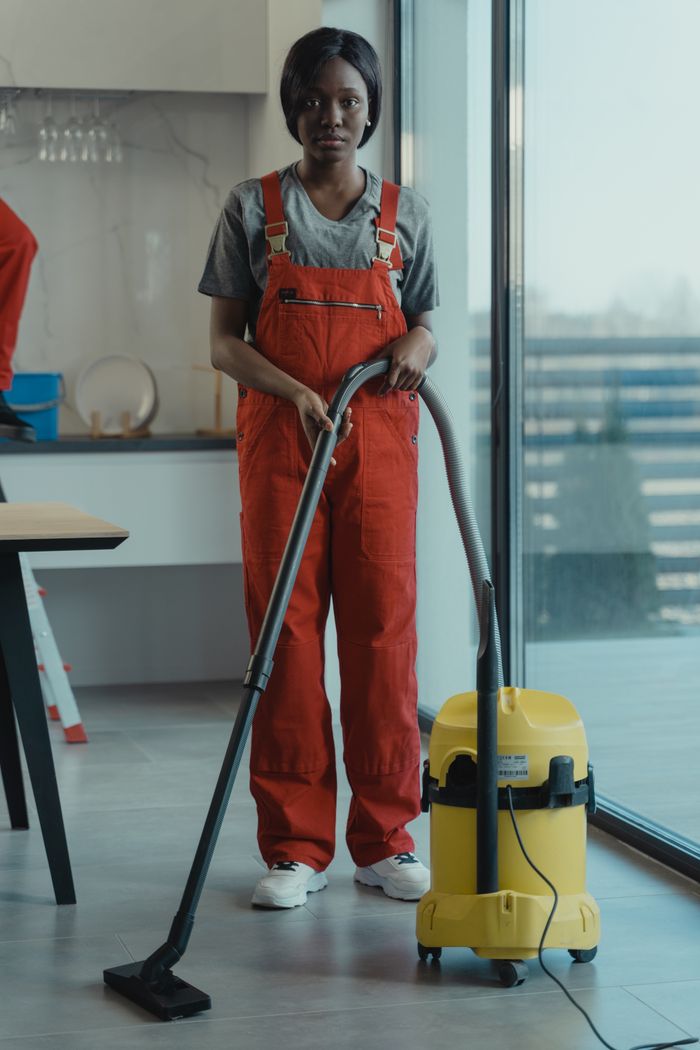 Une femme adulte vêtue d’une combinaison rouge utilise un aspirateur dans un intérieur moderne, concentrée sur les tâches de nettoyage.